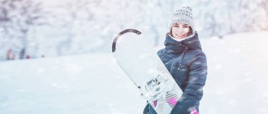 Kış günü snowboard yapmak. Beyaz yamaçta snowboard yapan genç bir kadın. Eğleniyor ve adrenalini hissediyor. Karla kaplı çam ağaçlarının muhteşem arka plan görüntüsü. Kışın kızı