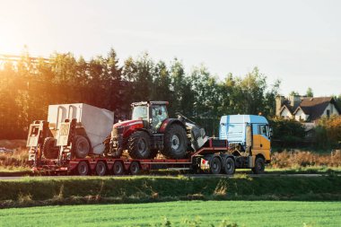 Kamyonet, bir kamyonla çiftlik malzemeleri taşıyor. Ağır endüstriyel kamyonun yarı tırı platformlu bir platformu taşıyordu. Yolda büyük bir modern tarım traktörü vardı. Akşam güneşi.