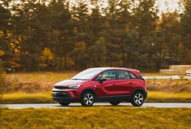 Yolda gün batımı: Doğanın manzaralı manzarasında asfalt yolda hızla giden kırmızı bir aile arabası.