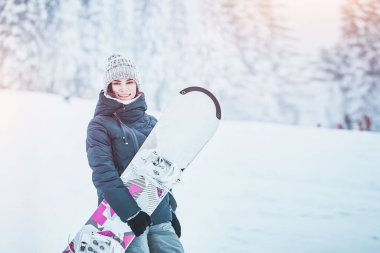 Snowboard 'u olan genç ve güzel bir kadın kış sporunu sever. Arka plan, kar fırtınası sırasında nefes kesici bir manzara. Dağlarda kar. Kar sporları ekipmanları kira.