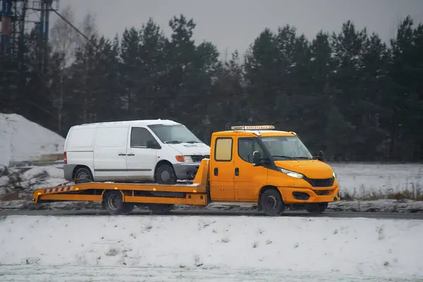 Car failure in winter: a tow truck transports a stranded vehicle on a snow-covered road. Dangerous driving conditions in a storm.