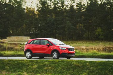 Yolda gün batımı: Doğanın manzaralı manzarasında asfalt yolda hızla giden kırmızı bir aile arabası.