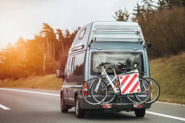 Bicycle on the camper van. Big modern white family RV camper truck with rear bike rack driving on the European highway.
