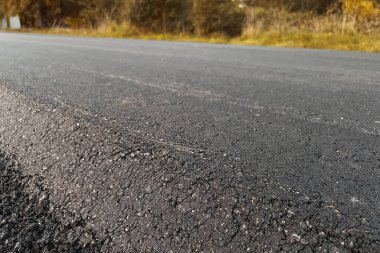 Yeni yoldaki taze sıcak asfaltın yakın çekim dokusu. Yol yapımı. Büyük bir katman taze asfalt. Sığ bir alan derinliğinde asfalt ham madde katmanı.