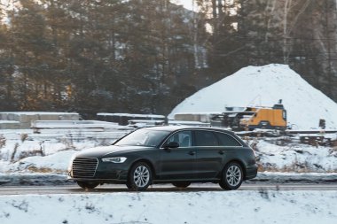 Kar fırtınası sırasında modern araba otoyola çıkıyor. Kışın yolda giderken arabanın yan görüntüsü. Kaygan ve soğuk hava koşullarında kış lastiklerinin gerekliliği. Sıfırın altında.