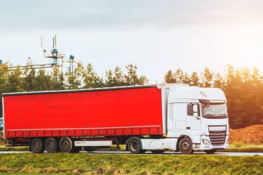 The sun sets over a beautiful landscape as a red truck transports a freight trailer on a motorway; a testament to the industry and business of transportation.