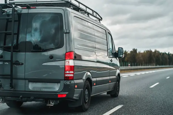 Camper van on the public road. Offroad modern van for traveling with a ladder on the back and an additional baggage roof rack on the top. Concept of road journey and adventures.