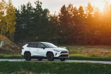 Modern bir aile arazi aracı görkemli bir doğa ve arka planda altın bir günbatımına sahip manzaralı bir yol boyunca seyahat eder. Daha fazla off-road kapasitesine ve 4WD AWD 4x4 moduna sahip subcompact kamyon.