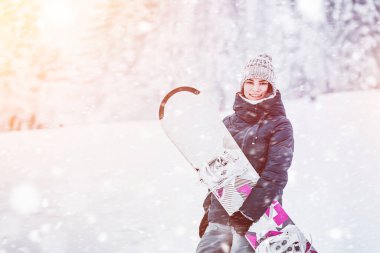Kış günü snowboard yapmak. Beyaz yamaçta snowboard yapan genç bir kadın. Eğleniyor ve adrenalini hissediyor. Karla kaplı çam ağaçlarının muhteşem arka plan görüntüsü. Kışın kızı