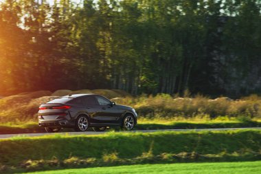 Alt kompakt bir SUV arabası arka planda muhteşem bir günbatımı ve dağlarla manzaralı kırsal bölgeleri keşfediyor..