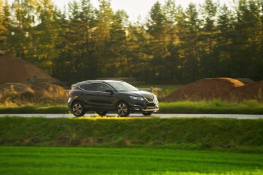 Modern ve lüks bir SUV, altın bir gün batımı gökyüzünün nefes kesici manzarasıyla asfalt bir yolda seyahat eder..