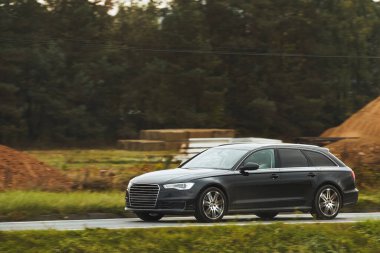 Büyüleyici alacakaranlık ışığı altında sakin bir orman manzarasının arka planında çekilmiş bir araba yolculuğu. Modern aile aracı otoyolda ilerliyor. Sürdürülebilir yolculuk.