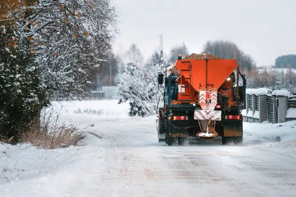 A Snow Plow Truck Clears the Road of Ice and Snow in Winter. Snow removal and adding Sand with Salt mixture to the Road. Snowplow outdoors clean pavement sidewalk road driveway. Winter weather.