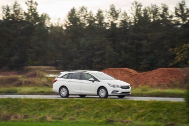 Büyüleyici alacakaranlık ışığı altında sakin bir orman manzarasının arka planında çekilmiş bir araba yolculuğu. Modern aile aracı otoyolda ilerliyor. Sürdürülebilir yolculuk.