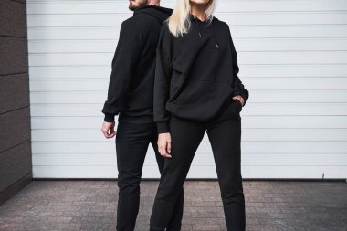 Modayı takip eden bir çift, model tasarım için siyah kapüşonlu açık havada poz veriyor. Baskı ve markalaşma için bir moda şablonu. Yüzü ve logosu olmayan sıradan ve zarif bir sokak kıyafeti..