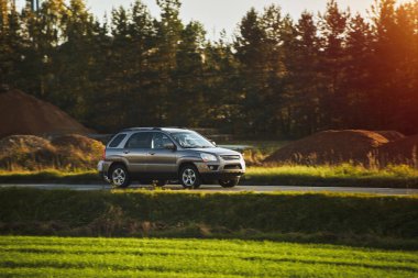 Modern ve lüks bir SUV, altın bir gün batımı gökyüzünün nefes kesici manzarasıyla asfalt bir yolda seyahat eder..
