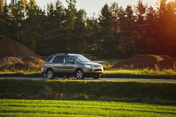 Modern ve lüks bir SUV, altın bir gün batımı gökyüzünün nefes kesici manzarasıyla asfalt bir yolda seyahat eder..