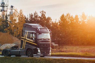 A powerful truck without a trailer speeds along a highway surrounded by industrial buildings and wild grass under a cloudy sky. Sustainable future global shipping.