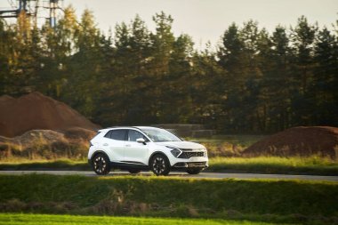 Melez bir SUV arabası görkemli bir doğa ve arka planda altın bir günbatımına sahip manzaralı bir yolda ilerliyor..