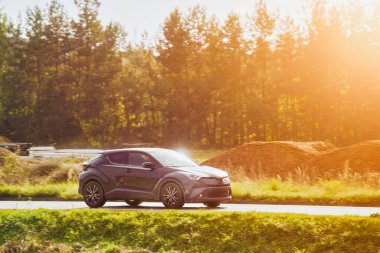 Melez bir SUV arabası görkemli bir doğa ve arka planda altın bir günbatımına sahip manzaralı bir yolda ilerliyor..