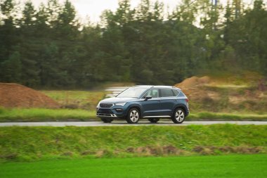 Alt kompakt bir SUV arabası arka planda muhteşem bir günbatımı ve dağlarla manzaralı kırsal bölgeleri keşfediyor..