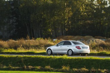 Bir Alman lüks arabası, gün batımının altın rengi ile sakin ormanı aydınlatan manzaralı bir güzergah boyunca sürüyor..