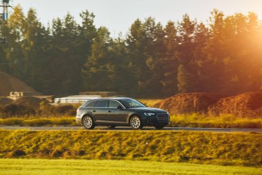 Büyüleyici alacakaranlık ışığı altında sakin bir orman manzarasının arka planında çekilmiş bir araba yolculuğu. Modern aile aracı otoyolda ilerliyor. Sürdürülebilir yolculuk.