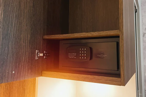 A digital safe with money and documents on a shelf in the closet. The safe is open and shows the keypad and the screen. The safe can be used at home or hotel for security and protection.