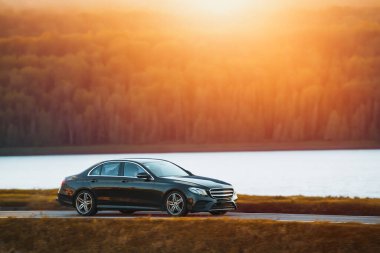 Şık ve hızlı bir Alman lüks arabası gün batımında manzaralı güzel bir yolda sürdürülebilir bir seyahat deneyimi yaşamaktadır..