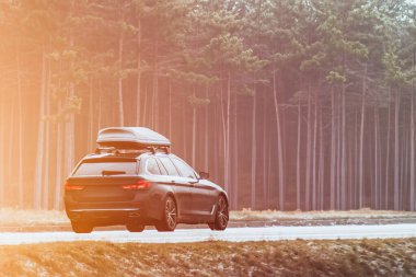 Çatıda siyah kargo kutusu olan siyah spor bir SUV araba manzaralı yolları keşfediyor. Araç kavramı kamp ve eğlence için hazır..