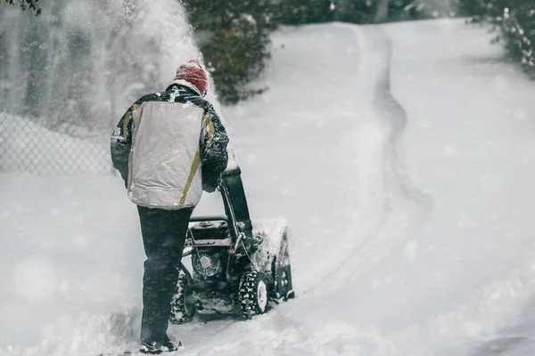 A man clears the snow from the street with a powerful snowblower after a heavy winter storm. Using a snowblower machine, a man works to remove the snowdrifts from the sidewalk in a snowy city.