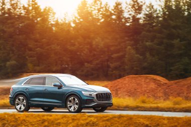 Modern ve lüks bir SUV, altın bir gün batımı gökyüzünün nefes kesici manzarasıyla asfalt bir yolda seyahat eder..