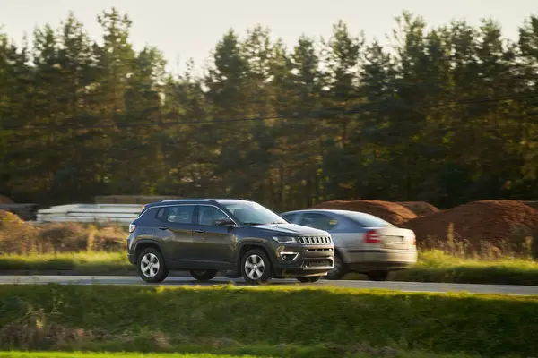 Melez bir SUV arabası görkemli bir doğa ve arka planda altın bir günbatımına sahip manzaralı bir yolda ilerliyor..