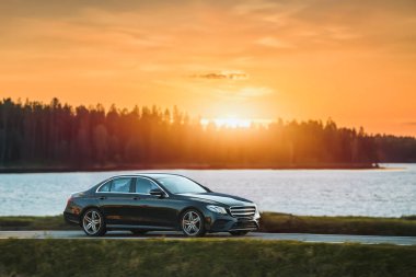 Bir Alman lüks arabası, gün batımının altın rengi ile sakin ormanı aydınlatan manzaralı bir güzergah boyunca sürüyor..