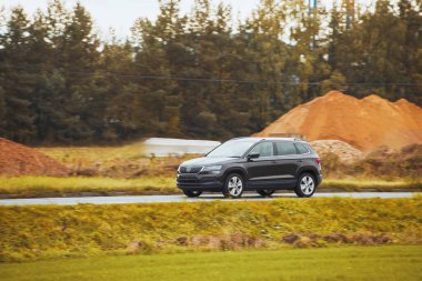 Melez bir SUV arabası görkemli bir doğa ve arka planda altın bir günbatımına sahip manzaralı bir yolda ilerliyor..