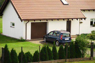 Beyaz duvarları ve kahverengi garaj kapısı olan iyi korunmuş bir evin arka planına park edilmiş bir aile arabası..