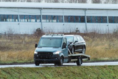 Siyah bir SUV, üzerinde bulutlu bir gökyüzü olan boş bir otoyol boyunca sarı bir çekiciyle taşınıyor..