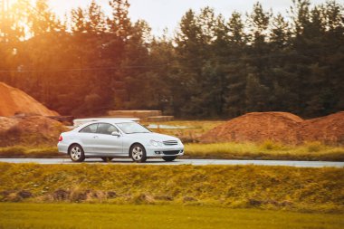 Bir Alman lüks arabası, gün batımının altın rengi ile sakin ormanı aydınlatan manzaralı bir güzergah boyunca sürüyor..