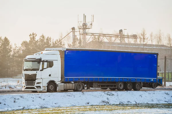 Transporting cargo on a snow-covered highway in winter. The transport truck drives a semi-trailer through a slippery and dangerous road. The weather is icy and snowy.