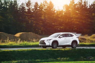 Modern ve lüks bir SUV, altın bir gün batımı gökyüzünün nefes kesici manzarasıyla asfalt bir yolda seyahat eder..