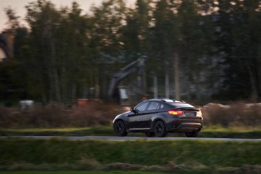 Bir Alman lüks arabası manzaralı bir yol boyunca sürer. Sportif bir araçla sürdürülebilir seyahat. Modern arabanın yan görüntüsü.