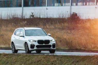 Melez bir SUV arabası görkemli bir doğa ve arka planda altın bir günbatımına sahip manzaralı bir yolda ilerliyor..