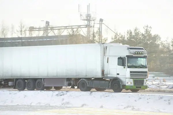 Truck in the winter. Large transport truck transporting commercial cargo in semi-trailer running on the winter snowy road. Snow-covered highway.