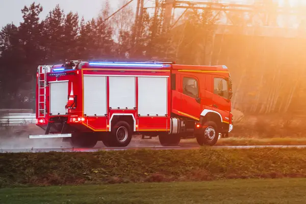 A vehicle with a siren drives to a fire. It is a firetruck with firemen and fire equipment.
