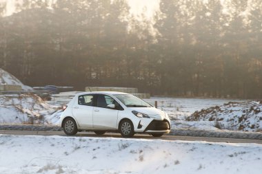Çarpıcı bir günbatımı ve ormanı olan virajlı bir yolda hızlı giden bir araba.