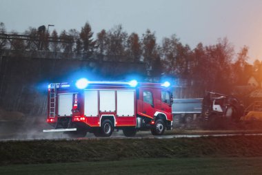 İtfaiyeciler itfaiye aracında iş başında. İtfaiye ekipmanı ve sirenli bir araç kullanıyorlar. İnsanlara yardım etme ve ateşle savaşma görevindeler..