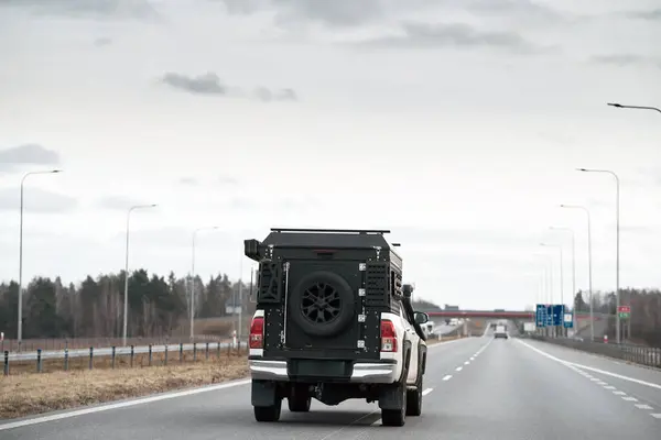 White pickup truck with a black box on the back driving down a highway. Truck has Off-Road package adds skid plates, mud flaps, all-terrain tires, and a suspension lift for better off-road capability.