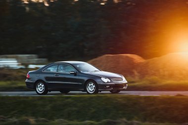 Modern bir Alman lüks otomobilinin zerafeti ve performansı, kırsal kesimde muhteşem bir yolda giderken yan manzarada sergileniyor..