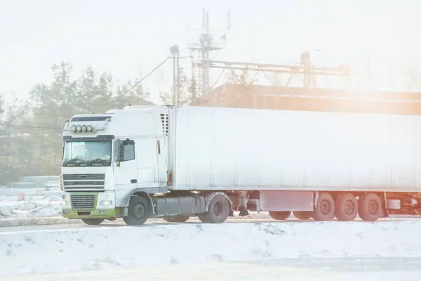 The snowy highway is a challenge for the transport truck. The semi-trailer delivers cargo to the shipping industry.