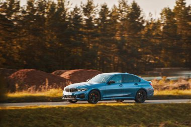 Bir Alman lüks arabası manzaralı bir yol boyunca sürer. Sportif bir araçla sürdürülebilir seyahat. Modern arabanın yan görüntüsü.